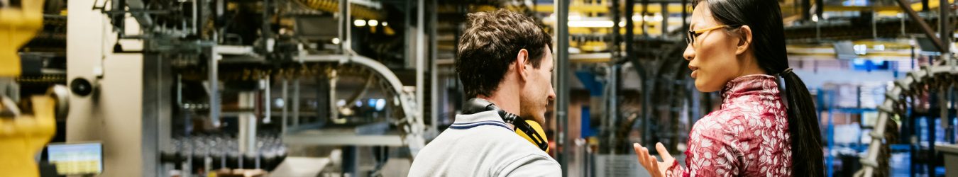 Mechanic and manager talking nearby a machine in a big printery about latest newspaper print