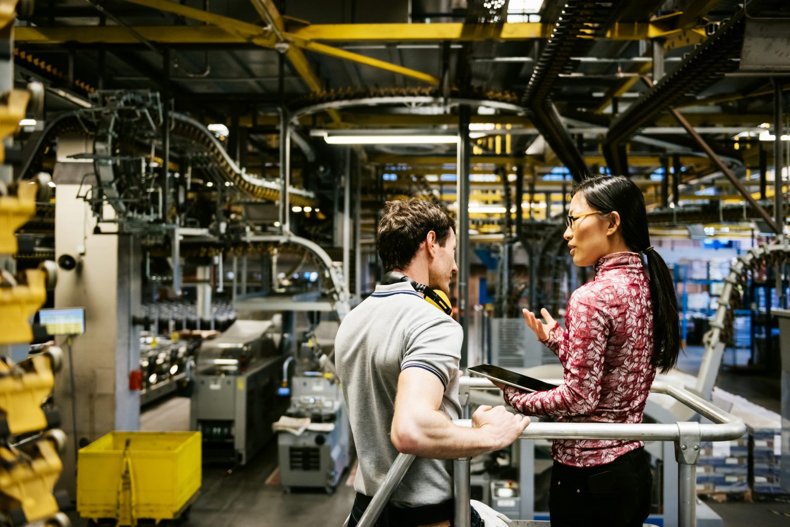 Mechanic and manager talking nearby a machine in a big printery about latest newspaper print