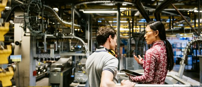 Mechanic and manager talking nearby a machine in a big printery about latest newspaper print