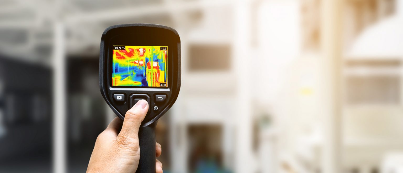 Technician using thermography camera to check temperature in factory