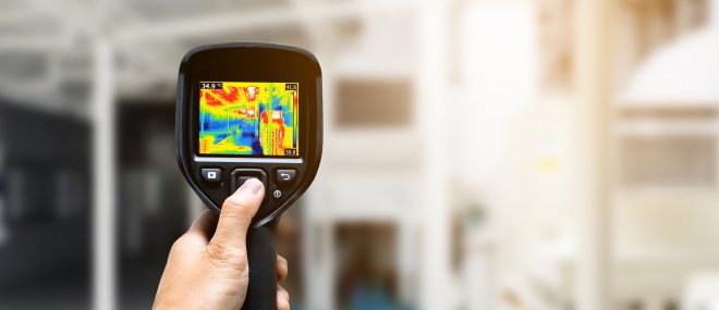 Technician using thermography camera to check temperature in factory