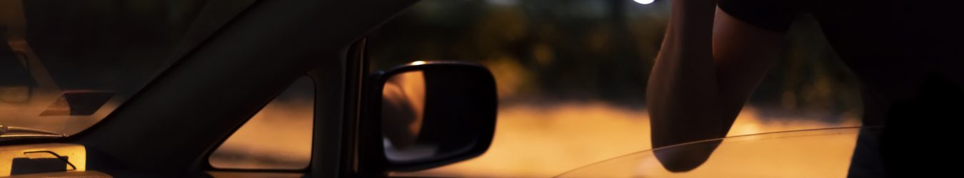 Car Robber with Flashlight looking into a car at night.