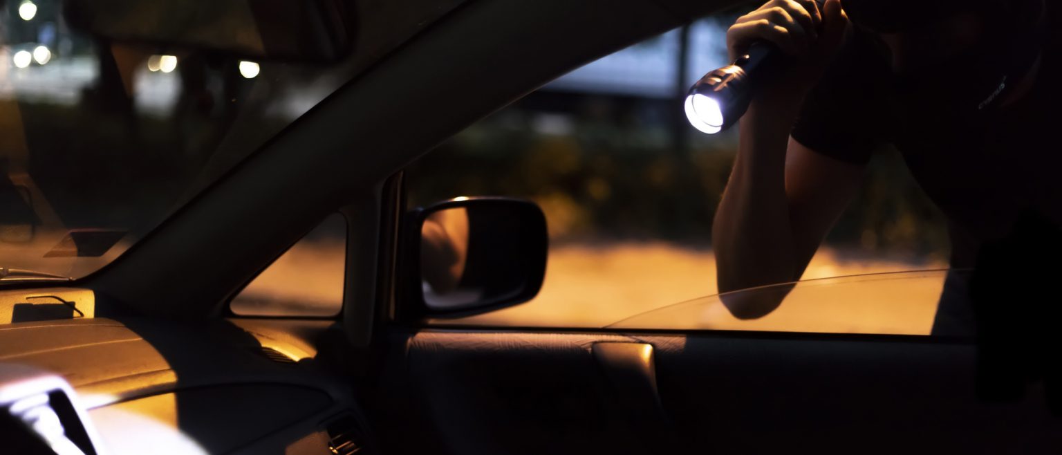 Car Robber with Flashlight looking into a car at night.