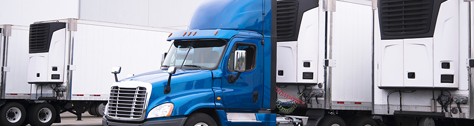 A semi-truck with a reefer trailer attached, exiting a warehouse parking lot.