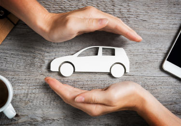 Two hands protecting car cutout over a wooden table.