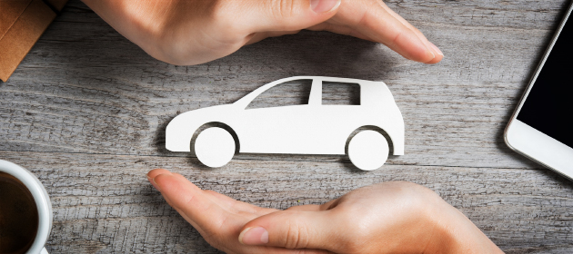 Two hands protecting car cutout over a wooden table.