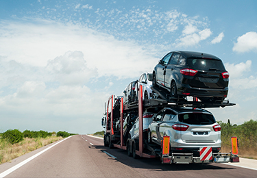 A truck with a car hauler trailer carrying a load of vehicles on a empty road.