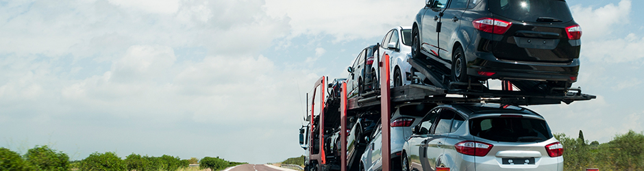 A truck with a car hauler trailer carrying a load of vehicles on a empty road.