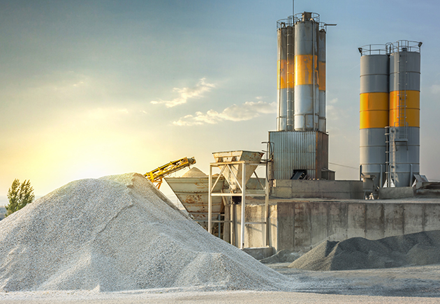 Concrete manufacturing plant with large piles of sand and gravel close by outside.