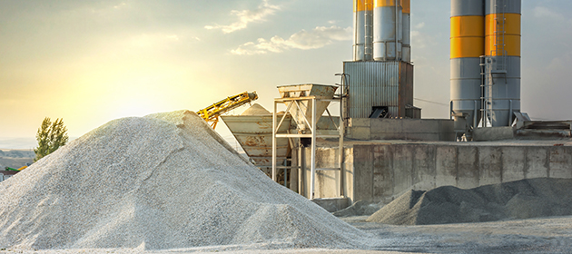 Concrete manufacturing plant with large piles of sand and gravel close by outside.