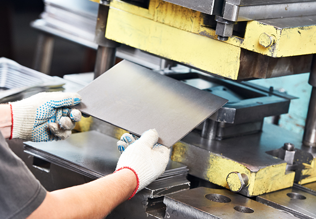 A person using a machinery press to work with a sheet of metal