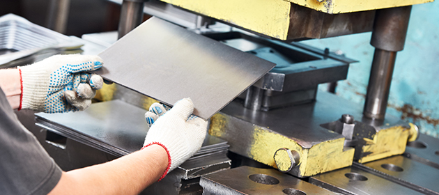 A person using a machinery press to work with a sheet of metal