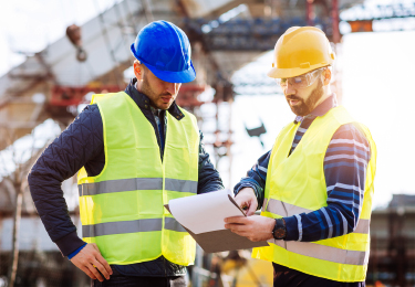 Two contractors looking at clipboard while on a construction site.