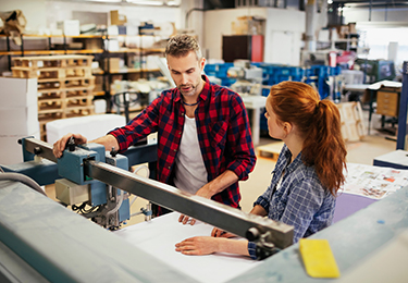 Two workers looking at a printing machine and talking.