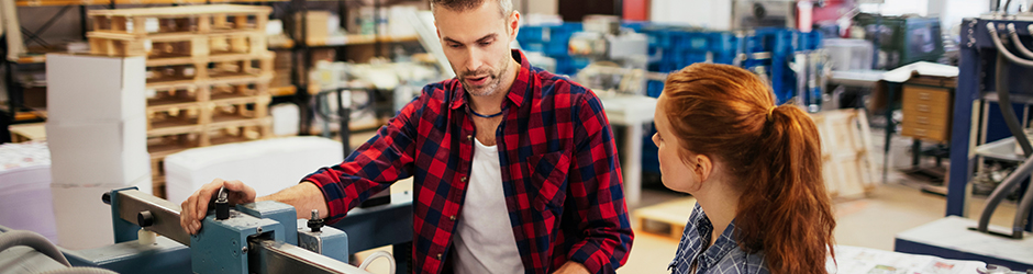 Two workers looking at a printing machine and talking.