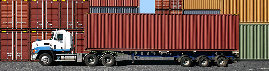 A freight container being loaded onto a truck at the docks.