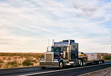 A long haul semi-truck carrying freight on a flatbed trailer.