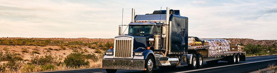 A long haul semi-truck carrying freight on a flatbed trailer.