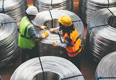 Two workers spooling metal wire in a manufacturing facility.