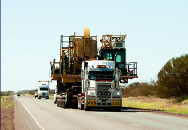 A white truck carrying a wide oversized cargo of heavy machinery.