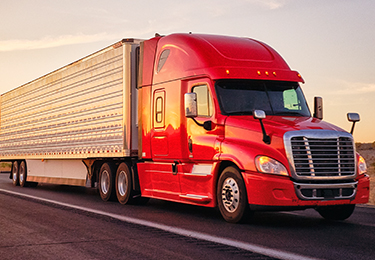 A big red rig semi-truck with an enclosed trailer transporting local goods on a roadway.