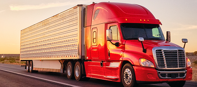 A big red rig semi-truck with an enclosed trailer transporting local goods on a roadway.