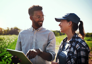 A businessman pointing to his tablet while talking to a female farmer.