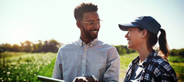 A businessman pointing to his tablet while talking to a female farmer.