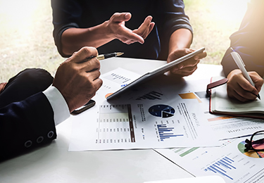 Business people in an office looking at a tablet while graphs charts are seen amongst them.