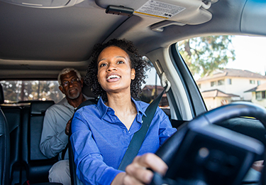 A female driver with a male passenger sitting in the back of a car.