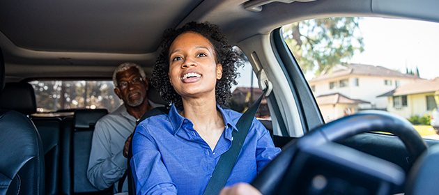 A female driver with a male passenger sitting in the back of a car.