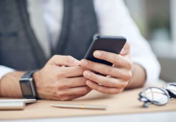 Close-up of unrecognizable businessman sitting at table and using mobile internet on smartphone