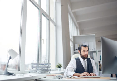 Busy male office manager sitting in light office and typing on computer keyboard