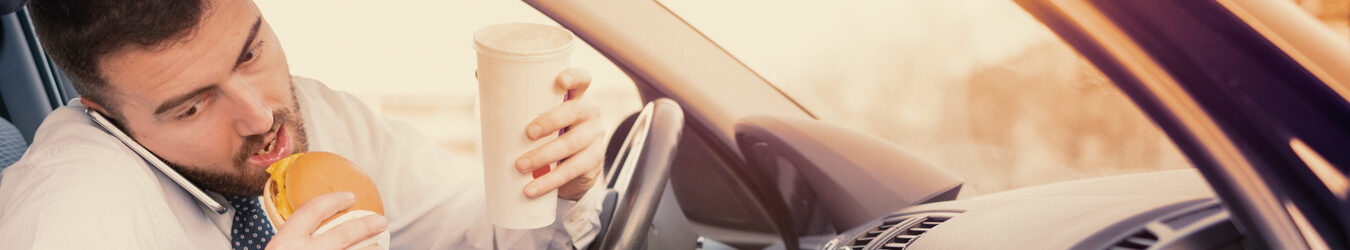 Man eating a hamburger and working seated his car