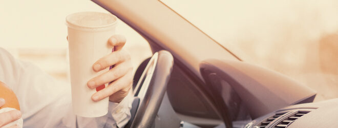 Man eating a hamburger and working seated his car