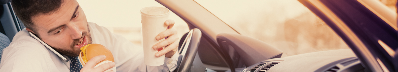 Man eating a hamburger and working seated his car