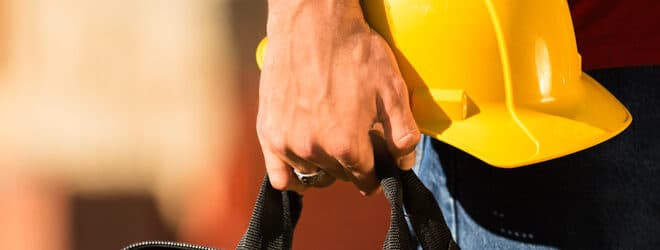 A construction worker holding tool box and a hard hat.