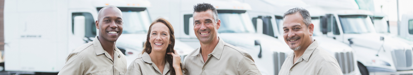 Four multi-ethnic workers in front of semi-trucks.