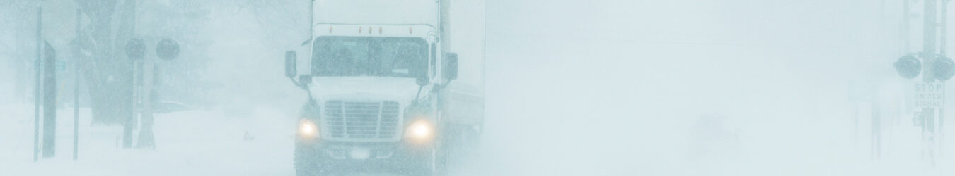 Semi-truck driving on a highway during a snowstorm