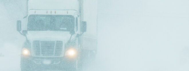 Semi-truck driving on a highway during a snowstorm