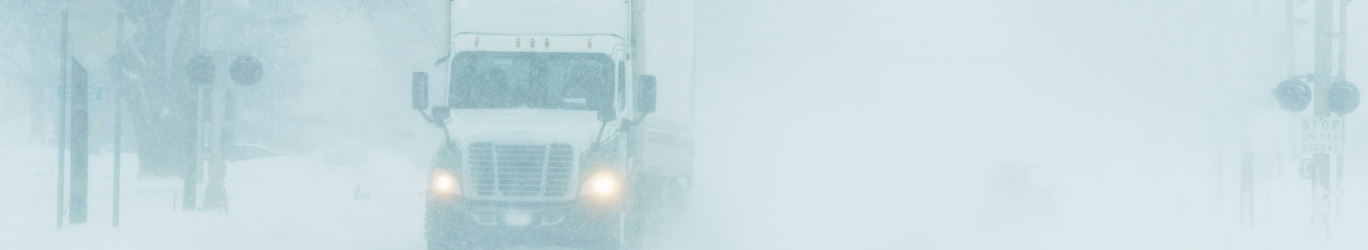 Semi-truck driving on a highway during a snowstorm
