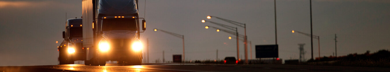 Two Semi diesel trucks on a highway at dusk.