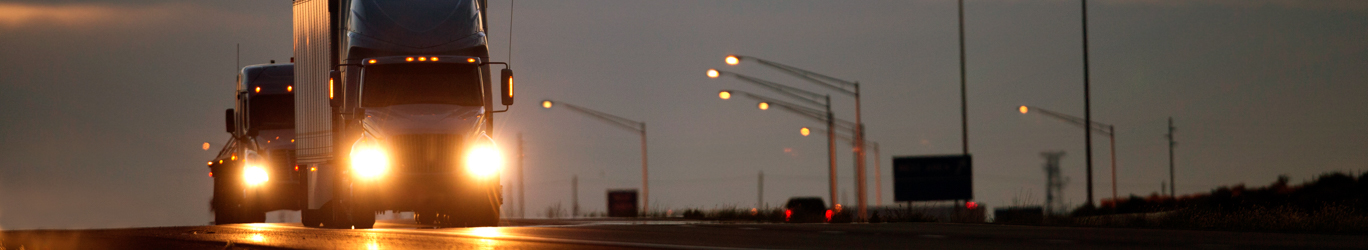 Two Semi diesel trucks on a highway at dusk.